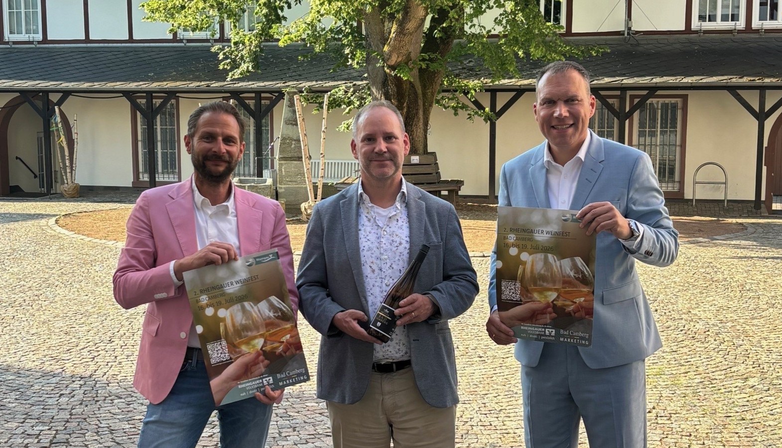 Zu sehen ist: Dominik Russler, Kurdirektor Michael Sinn und Bürgermeister Daniel Rühl im Amthof-Innenhof mit dem Weinfest-Plakat